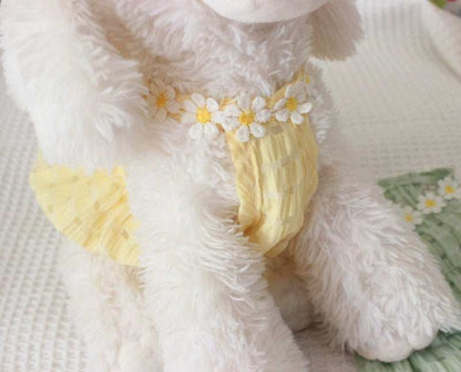 Close-up of a fluffy white lamb toy with yellow legs and floral decorations on a soft surface.