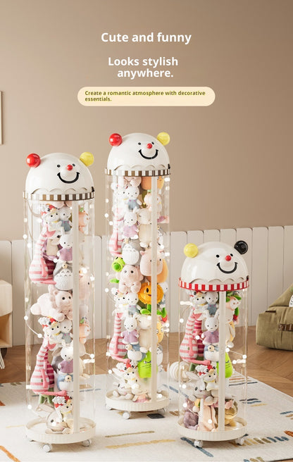 Three clear cylindrical plush toy storage cabinets with smiling snowman-style tops, filled with stuffed animals, shown in a styled room setting with warm beige walls and text at the top.