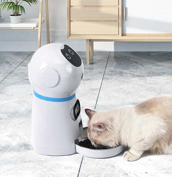 Pet robot feeder dispensing food to a cat on a tiled floor.