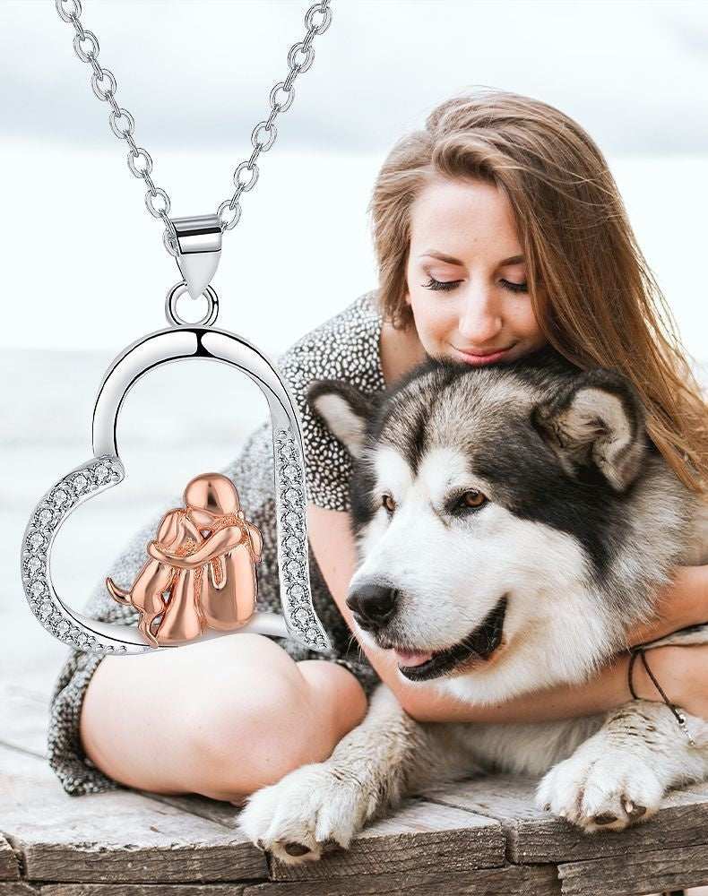 Woman holding a dog with a heart-shaped necklace featuring a small dog figure.
