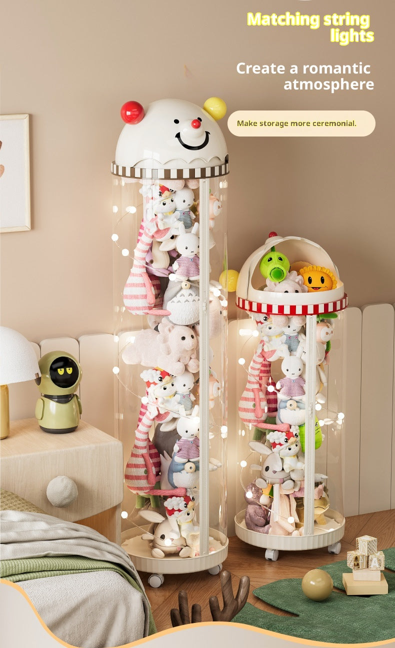 Two decorative hanging string light display stands filled with plush toys in a softly lit bedroom or playroom. The larger left stand is a tall clear cylinder with a white smiling character head on top and warm fairy lights draped inside.