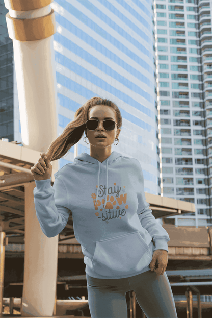 Young woman wearing Stay Pawsitive Unisex Hoodie light gray with paw print design and sunglasses in city