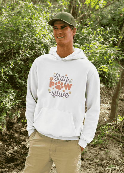 Smiling man outdoors wearing a white Stay Pawsitive Unisex Hoodie with paw graphic on chest and kangaroo pocket